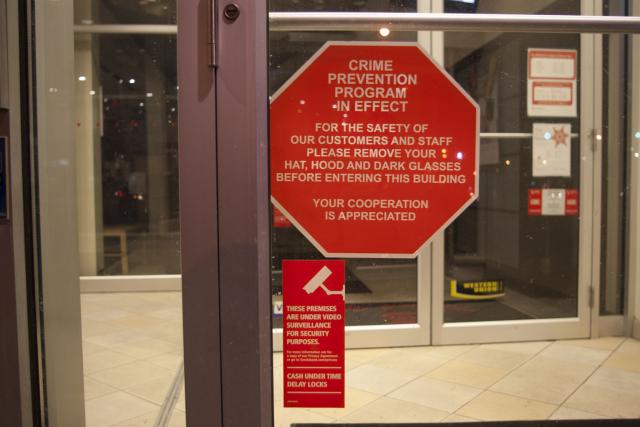“Crime prevention program in effect: For the safety of our customers and staff, please remove your hat, hood and dark glasses before entering this building. Your cooperation is appreciated.”